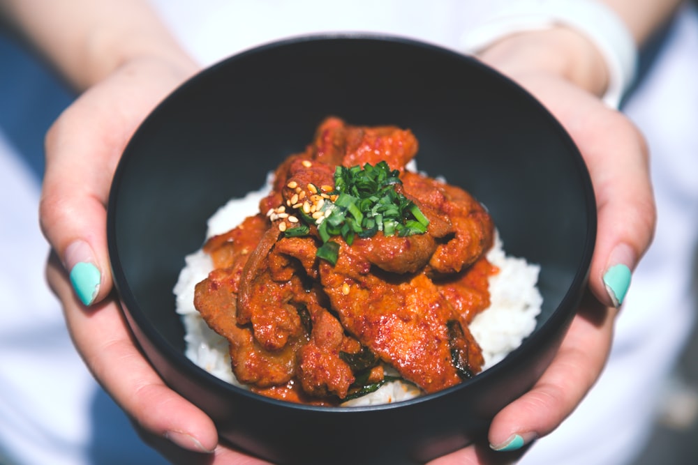 Stock photo of hands holding a bowl of spicy pork over rice — placeholder, not their kitchen